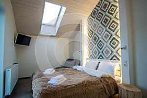 Interior of a spacious hotel bedroom on attic floor with fresh linen on a big double bed. Cozy contemporary mansard room in a