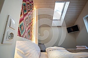 Interior of a spacious hotel bedroom on attic floor with fresh linen on a big double bed. Cozy contemporary mansard room in a