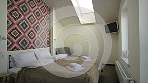 Interior of a spacious hotel bedroom on attic floor with fresh linen on a big double bed. Cozy contemporary mansard room in a mode