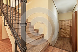 Interior staircase of a duplex residential house with gray tile steps, metal railing and Castilian-style paneled wooden access