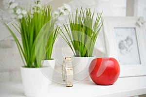Interior in the studio, green grass in white pots and a red apple