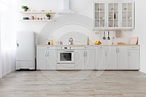 Interior of stylish kitchen with light walls, white furniture with utensils and fruits