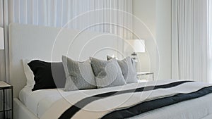 Interior of stylish suite with made double bed with soft headboard between nightstands with lamps covered with layers of