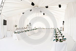 Interior of tent for wedding diner, ready for guests. Served round banquet table outdoor in marquee decorated hydrangea