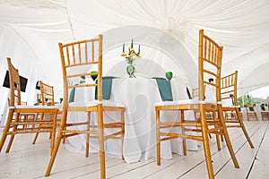 Interior of tent for wedding dinner, ready for guests. Served round banquet table. Golden dishes, green wine glasses and