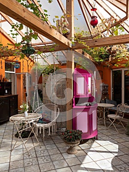 Interior of veranda. Cozy space in patio. A lot of plants. Orange wall. Wooden furniture. Hanging wicker white chair.