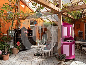 Interior of veranda. Cozy space in patio. A lot of plants. Orange wall. Wooden furniture. Hanging wicker white chair.