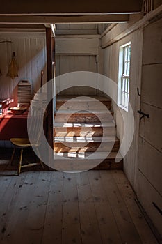Interior of a very old fishing shack, light streaming through window onto stairs, table and chair