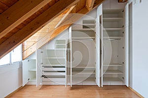 Interior view of a custom-made closet with open doors built into a master bedroom with a sloping roof