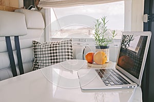 Interior view of modern camper van vehicle with emptu elegant white table and laptop on it. Concept of vacation and home to live