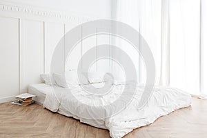 Interior view of unmade messy bed on a wooden floor in the morning with curtain and sunlight