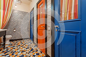 Interior of vintage style toilet room with old wooden doors to bathroom. Blue and red doors over colorful floor tiles