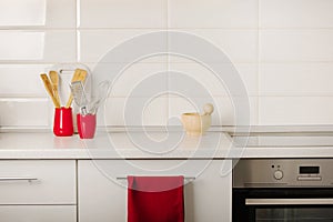 Interior white kitchen with kitchen tools and red crockery.