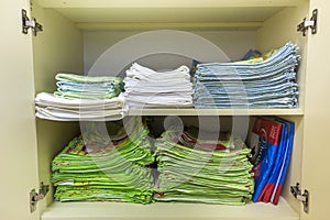 Interior of white plastic cabinet or clothing wardrobe with open doors with stacked pile of clean colorful linen. Household and