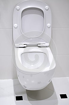 Interior. A white toilet bowl hangs on a white tile wall in a white bathroom