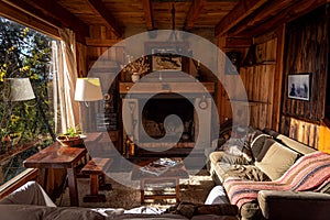 Interior of a wooden cozy cabin with comfortable couches around the fireplace, with country decoration, illuminated by