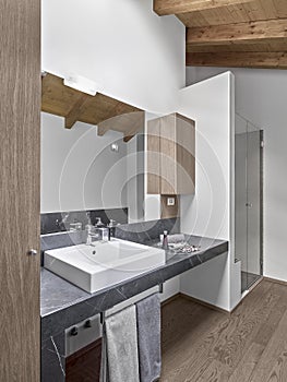 Interiors of a modern bathroom in the attic room with wooden  beamed ceiling and the wooden floor