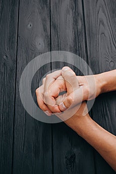 Interlocked fingers, white male hands interlocked on black rustic wood table close up. top view. a man is waiting for negotiations