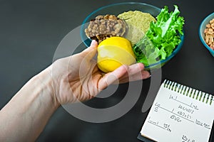 Intermittent fasting. Apple in hand and healthy food on a plate with greens