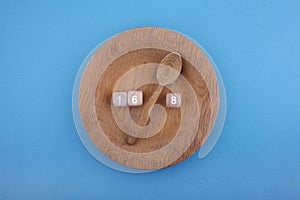 Intermittent Fasting. Wooden spoon between wooden dice with numbers 16 and 8 on plate. Health and fitness trend.