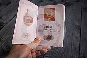 Internal passport of the Russian Federation in a woman`s hand on a blurred wood background.