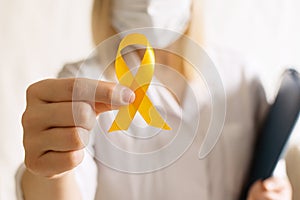 International Childhood Cancer Day. Female doctor in coat holds yellow ribbon on white background. Sarcoma Awareness, Bone cancer