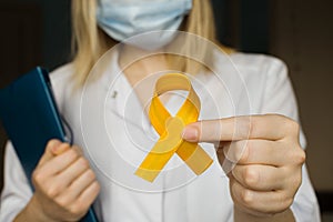 International Childhood Cancer Day. Female doctor in white coat holds yellow ribbon. Sarcoma Awareness, bladder cancer. Leukemia