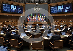 International delegates sit in a modern UN-style conference hall with national flags flying for a global meeting or formal summit. photo