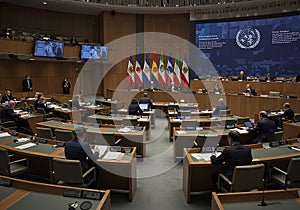 International delegates sit in a modern UN-style conference hall with national flags flying for a global meeting or formal summit. photo