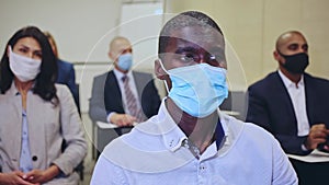 International group of business people wearing protective face masks listening to presentation in conference room.