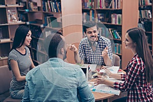 International group of four cheerful clever young students bookworms studying in the ancient university library, sit at the table