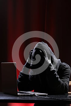 International hacker in black pullover and black mask trying to hack government on a black and red background. Cyber crime .