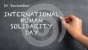 International Human Solidarity Day, 20 December. Woman`s hand with white chalk