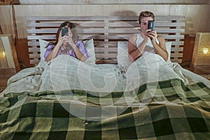 Internet addict couple on bed ignoring each other using social media app on mobile phone flirting and on line dating in relationsh