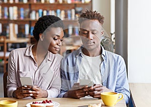 Internet addiction. Millennial black guy and girl looking at mobile phones on dull date at cafe