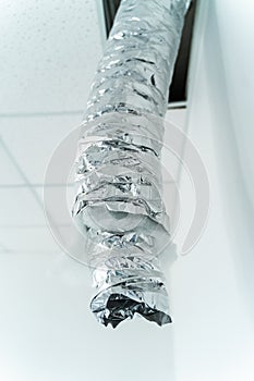 Internet cable in foil hangs from the ceiling. Empty industrial facility with grey wall. Air conditioning tube. Closeup photo