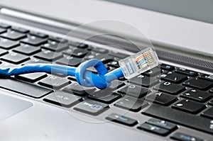 Internet cable tied into knot lying on computer keyboard symbolizing network or connectivity problems