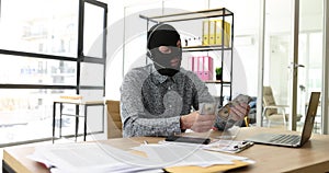 Internet operator scammer in a balaclava with headphones with microphone counts money at computer desk