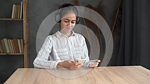 Internet order and e-commerce concept. Smiling woman using smartphone and holding credit card while sitting at table at