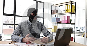 Internet scammer in balaclava with headphones with smartphone and bank card in office