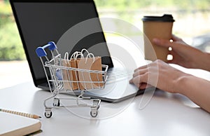 Internet shopping. Small cart with bags near woman using laptop indoors