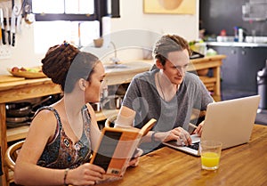 Internet trumps book every time. a happy couple with dreadlocks sitting at a table using a laptop and reading a book. photo