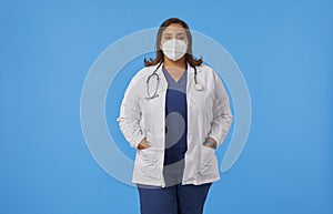 Internist woman with a protective face mask and hands on pocket of medical coat looking at camera