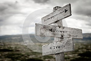 Interpretation, power and truth text on wooden rustic signpost outdoors in nature/mountain scenery.