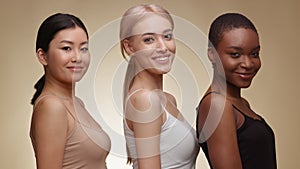 Interracial beauty. Profile portrait of mixed ladies turning faces to camera and smiling, posing over beige background