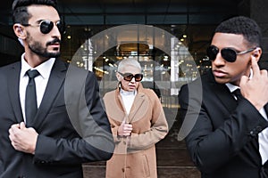 interracial bodyguards in sunglasses escorting senior