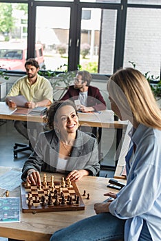Interracial businesswomen playing chess near blurred