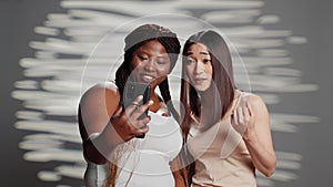 Interracial cheerful ladies taking photos with phone