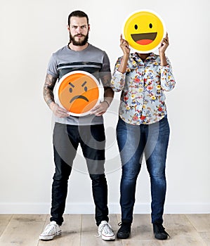 Interracial couple holding an expressive emoticon face facial expression frown and smile relationship issue concept