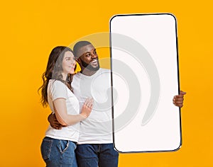 Interracial couple showing big white empty smartphone screen